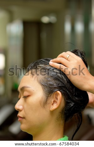 Asian ethnic young woman having hair treatment massage at hairdressing salon