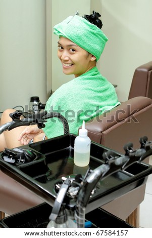 Happy Asian ethnic young woman having hair spa treatment at salon