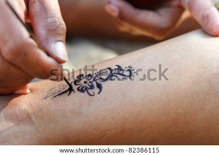 closeup of an artist hand drawing temporary tattoo on someone leg