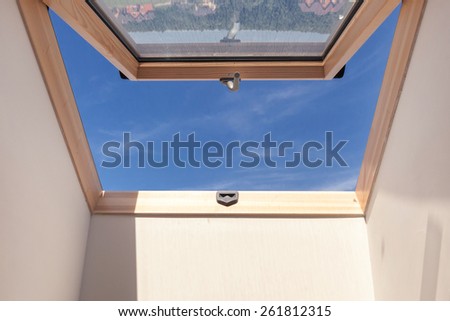 Opened roof window dormer with white wall against blue sky