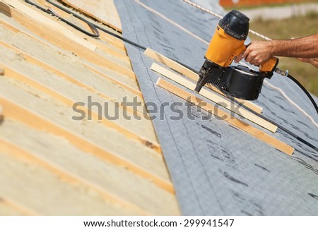 Building contractor worker (roofer) with a air nail gun nailer working on the roof  on a new home constructiion project
