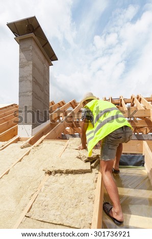Roofer builder worker installing roof insulation material. New house under construction with chimney