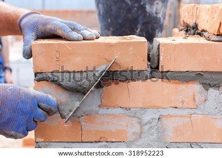 Construction mason worker bricklayer installing red brick with trowel putty knife outdoors