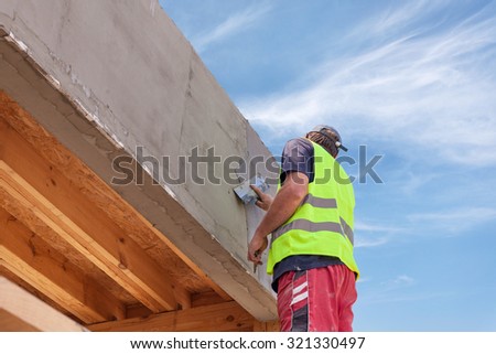 Construction worker with trowel plastering a facade of a new house