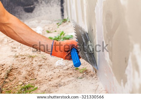 Construction worker plastering a wall and house foundation with trowel