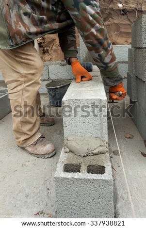 Construction mason worker bricklayer  laying concrete block foundation wall with spatula outdoors