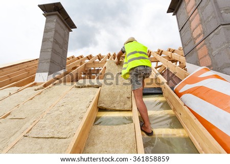 Roofer builder worker installing roof insulation material (rockwool) on new house under construction