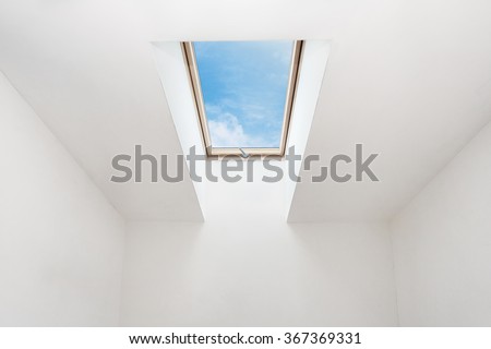 A modern open skylight (mansard window) in an attic room against blue sky