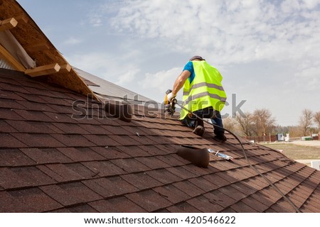 Construction worker putting the asphalt roofing (shingles) with nail gun on a large commercial apartment building development