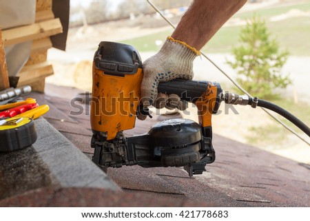 Construction worker putting the asphalt roofing (shingles) with nail gun on a large commercial apartment building development