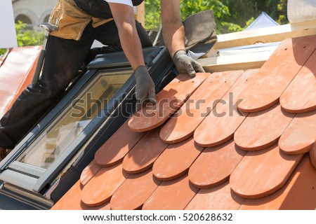 Hands of roofer laying tile on the roof. Installing natural red tile. Roof with mansard windows.