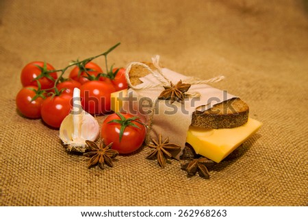 Sandwich with cheese wrapped in paper, cherry tomatoes and garlic on old cloth