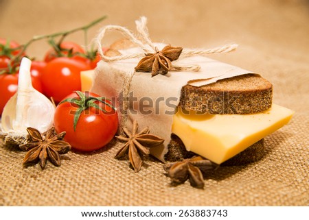 Sandwich with cheese wrapped in paper, cherry tomatoes and garlic on cloth