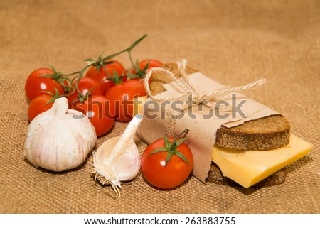 Sandwich with cheese wrapped in paper, cherry tomatoes and garlic on cloth