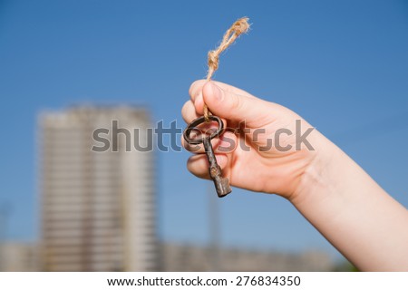 Child hand holding an old key on a string against the sky