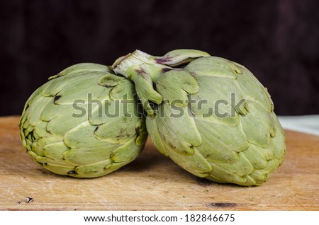 Two fresh artichokes with stem and leaf and a half showing the heart