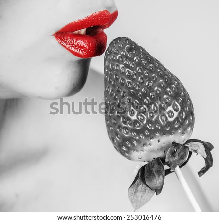 A creative portrait of a sensual girl holding a red juicy strawberry near her tasty lips.