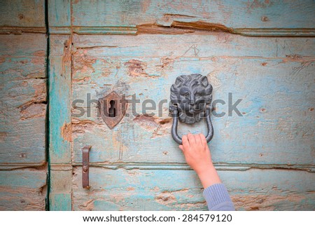 Hand of a person who knocks at a door knocker in the shape of medieval lion, hoping to be accepted.