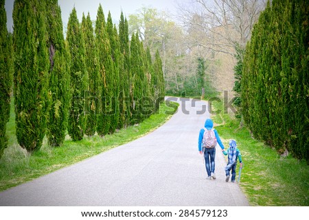 Mother and son holding hands run through a driveway lined with cypresses backpacking along a journey that will travel together for life.