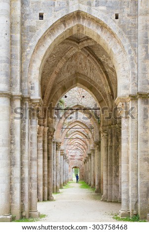A person is around isolated in the background of towering aisles arches of an old cathedral ruins.