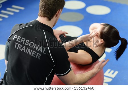 Personal Trainer Helping Young Woman In Gym With Crunching Exercises