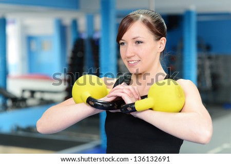 Young woman working out with kettle bell weights, with personal trainer in gym