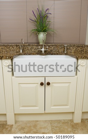 Modern contemporary kitchen interior with granite worktop and cream units, focus on the sink area.