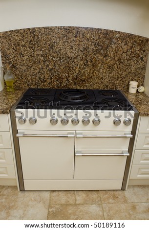 Large range style cooker in modern kitchen interior with granite worktop and cream units