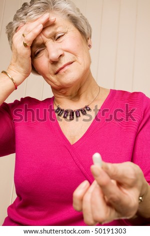 Senior older lady holding a pain relief tablet or pill, while holding her head with her hand in discomfort