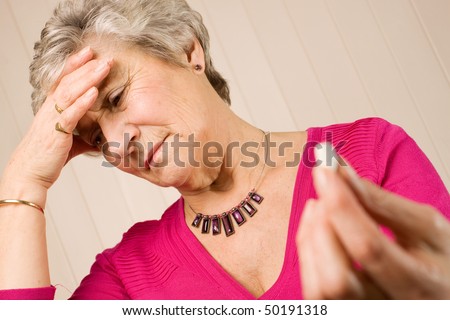 Senior older lady holding a pain relief tablet or pill, while holding her head with her hand in discomfort