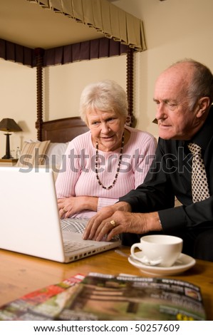 Happy senior couple using laptop in luxurious hotel bedroom suite