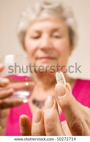 Senior mature lady holding a tablet or pill in one hand and a glass of water in the other