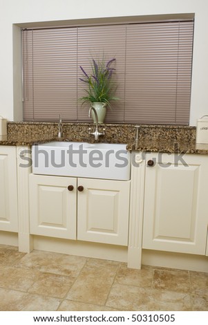 Modern contemporary kitchen interior with granite worktop and cream units, focus on the sink area.