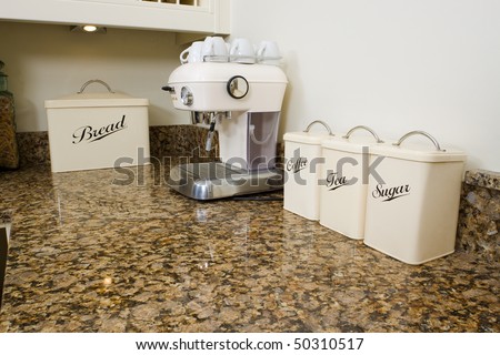 Tea, coffee and sugar pots in a modern kitchen interior with granite worktop and cream units