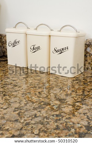 Tea, coffee and sugar pots in a modern kitchen interior with granite worktop and cream units