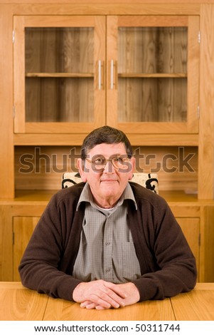 Serious senior man sitting at wooden table with copyspace above