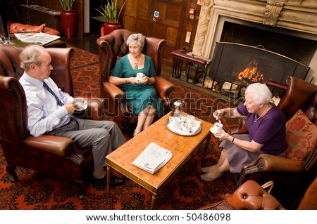 A group of older senior friends enjoying tea and talking in hotel lounge area