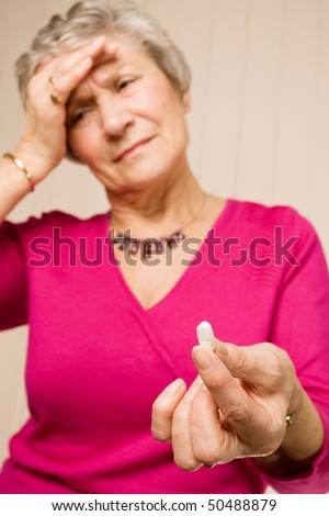 Mature older lady holding a pain relief tablet or pill, while holding her head with her hand in discomfort