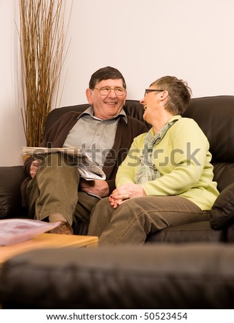 Senior man and woman couple laughing together sitting on sofa in lounge