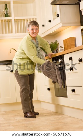 Happy older senior woman using cooker in modern designer kitchen