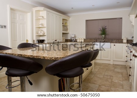Modern contemporary kitchen interior with granite worktop and cream units and black stools