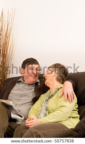 Senior man and woman couple reading newspaper sitting on sofa in lounge, with copyspace above