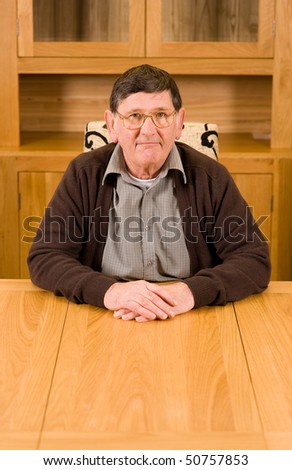 Serious looking senior man sitting at wooden table with copyspace below