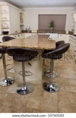 Modern contemporary kitchen interior with granite worktop and cream units and black stools