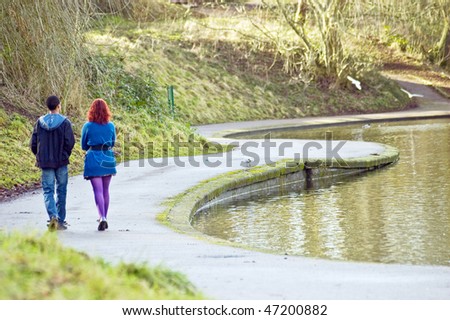 a young mixed race couple walking along a lake in a park in the spring-time.