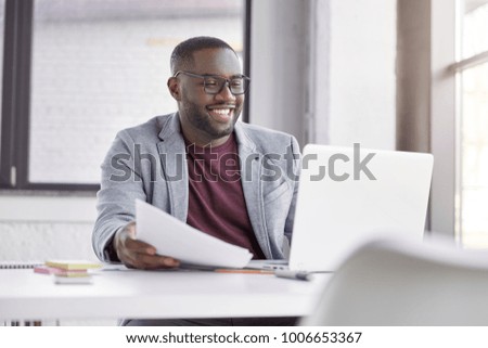 Smiling black male restaurater makes financial report and does shopping online, buys products for restaurant, studies annual figures, analyzes profits. Enterprise owner checks status of bank account