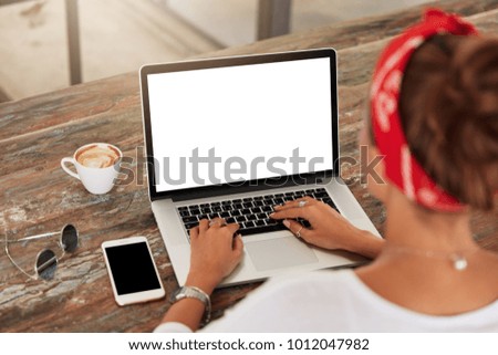 Back view of unrecognizable female model advertizes news and keyboards on laptop computer with balnk copy screen for your advertising content. Woman`s hands types information on internet websites