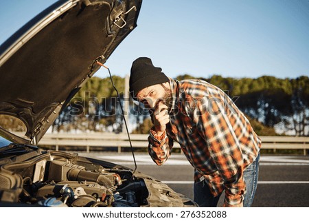 Car driver young man stands a thoughtful expression face and looking at camera on road trip in summer. Transportation and vehicle concept model male opening car bonnet on freeway going to sea in Spain
