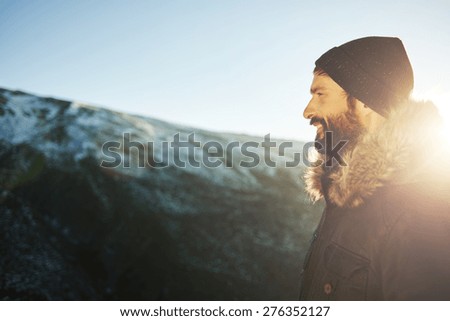 Hiker on top of the mountain enjoying sunrise. Happy smiling bearded  traveler looking into the distance at sunset. In the background is a beautiful view of snow mountains.