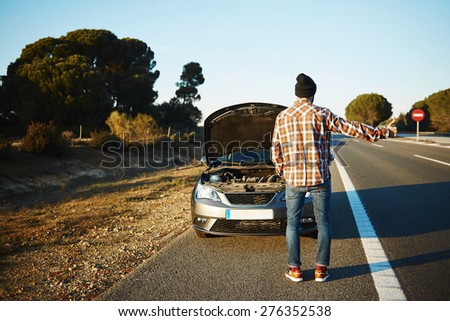 Cars - driver trying stop car in travel because his car broken. Young man stand on freeway and shows thumbs up. Young interracial man in their twenties, Caucasian man.